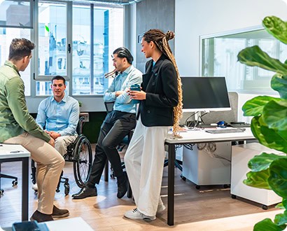 Business people having a conversation in a modern office, one of their colleagues using a wheelchair demonstrating inclusion and diversity in the workplace.